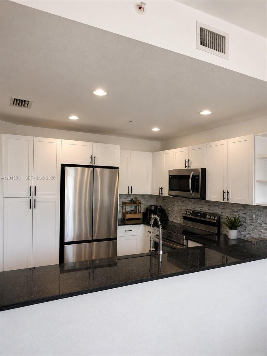 A kitchen features white cabinetry, stainless steel appliances, and a black granite countertop — 10885 NW 89th Ter # 203, Doral FL 33178, DORAL, FL