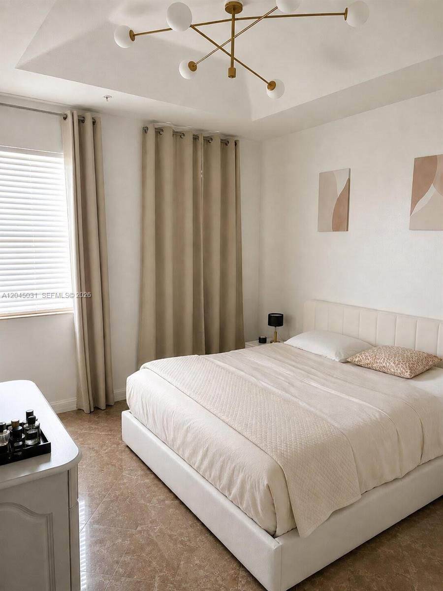 A bedroom features a white upholstered bed, neutral curtains, and a modern gold chandelier — 10885 NW 89th Ter # 203, Doral FL 33178, DORAL, FL