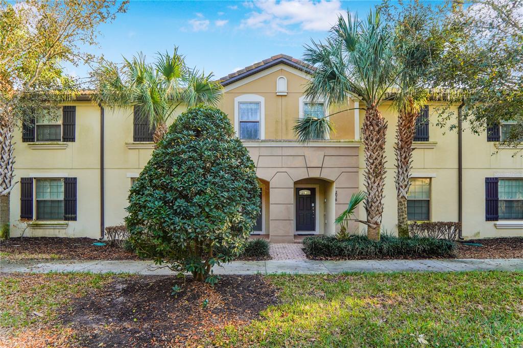 A two-story townhouse exterior with tan stucco walls, dark shutters, and a central entryway — 2022 MAJORCA DRIVE, KISSIMMEE, FL