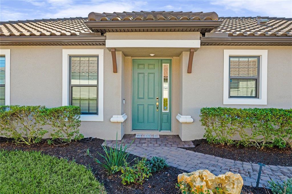 A teal front door with a sidelight is centered on the beige exterior of a house — 4743 MOTTA COURT, BRADENTON, FL