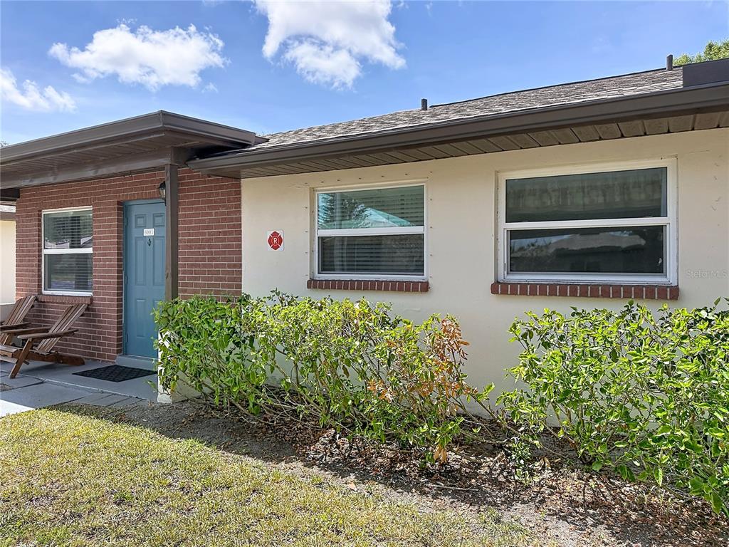 The exterior of a single-story home features a brick entrance, blue door, and two windows — 24862 US HIGHWAY 19 N UNIT 3001, CLEARWATER, FL