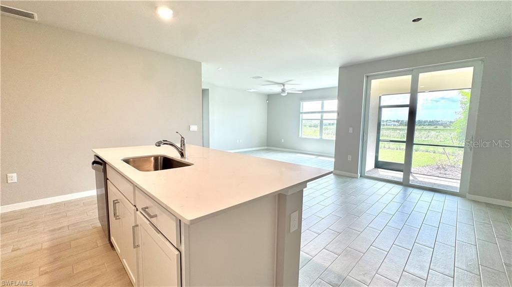 A kitchen island with a sink sits in an open-concept room with tile flooring — 17710 SHADE TREE LOOP, PUNTA GORDA, FL