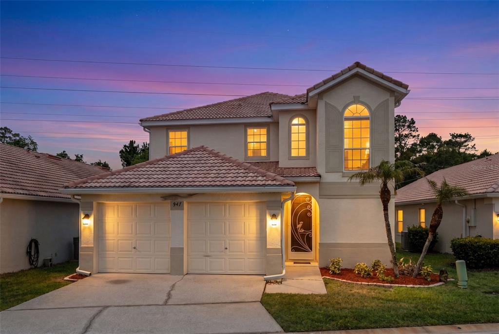 A two-story stucco house with a tile roof and a two-car garage at dusk — 947 GLEN ABBEY CIRCLE, WINTER SPRINGS, FL