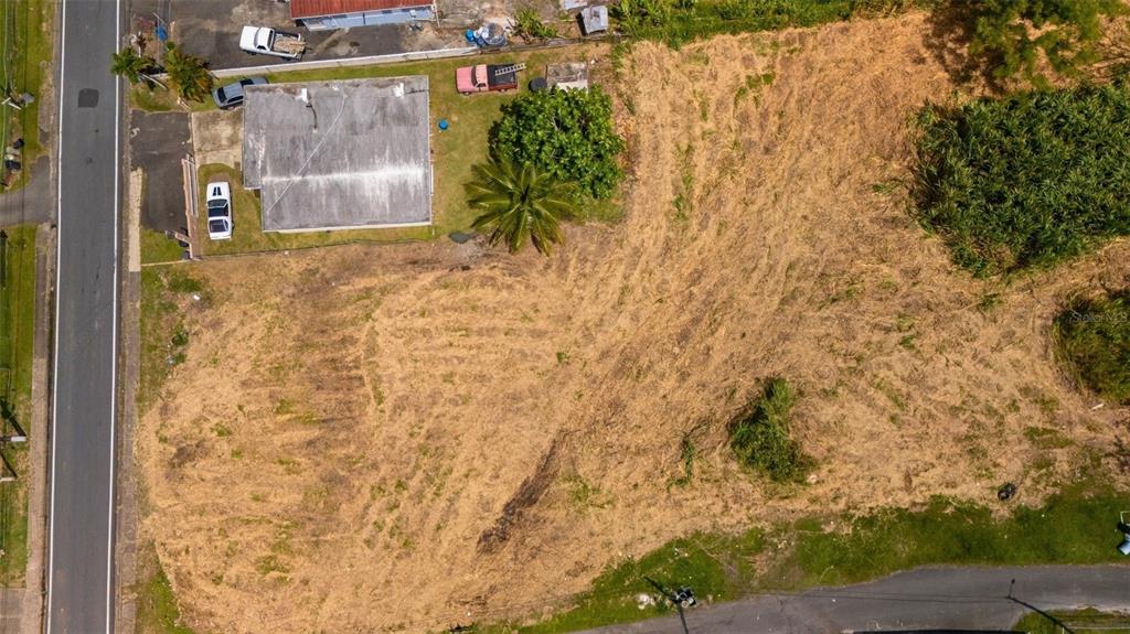 An aerial view shows a vacant, cleared lot adjacent to a house and two roads — BO CEIBA NORTE 28 COM SANTANA, JUNCOS, PR