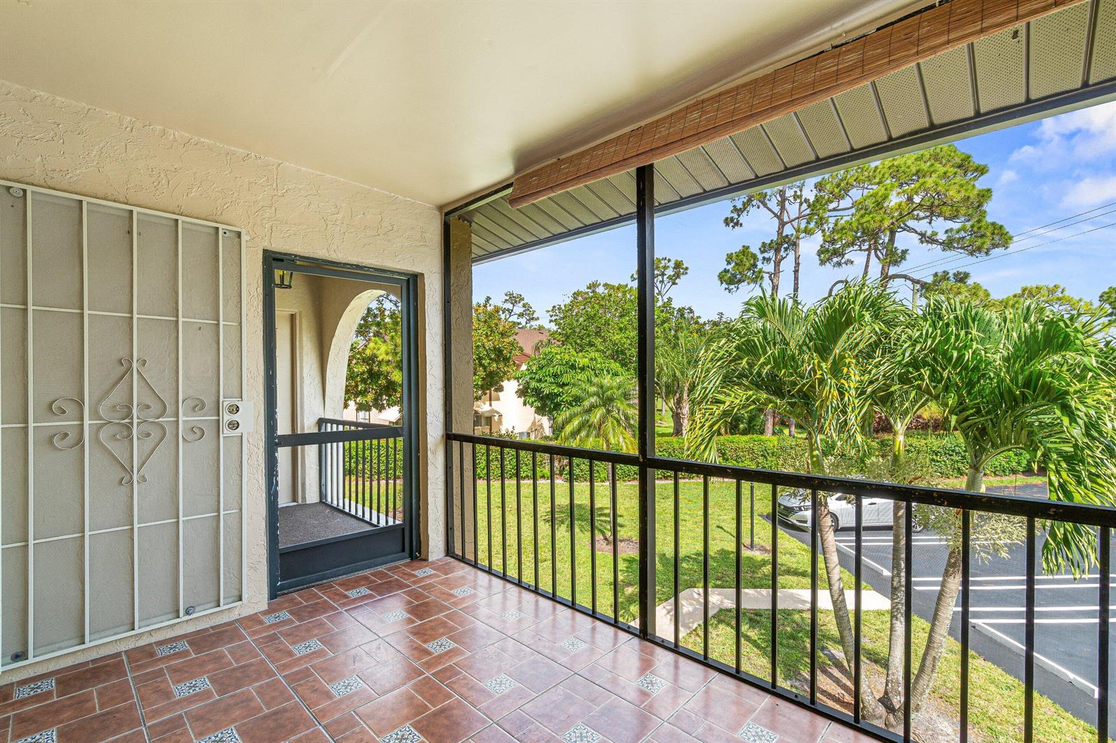 A tiled, screened-in balcony overlooks a parking lot and green space with palm trees — 223 Pine Hov Circle # 2, FL 33463, FL
