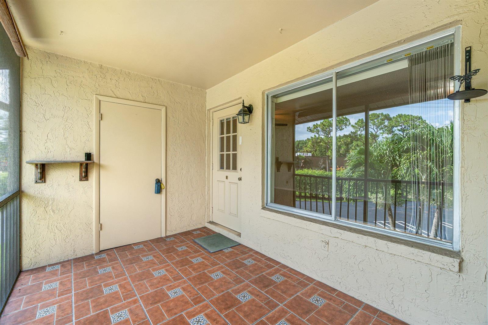 A covered patio features tiled flooring, a solid door, a glass-paneled door, and a large window — 223 Pine Hov Circle # 2, FL 33463, FL