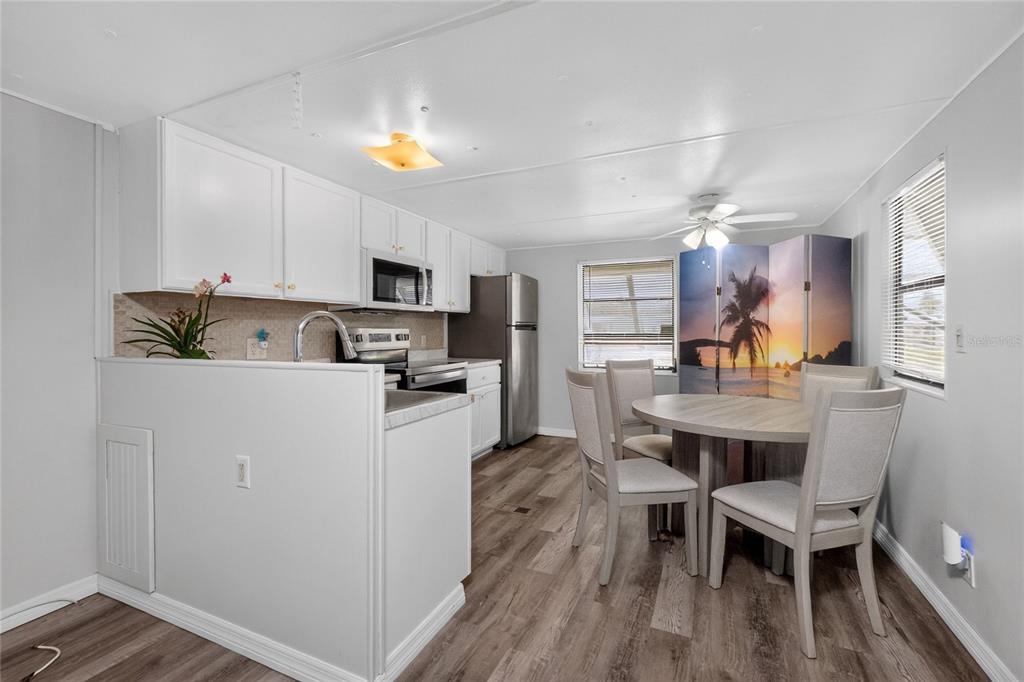 A kitchen and dining area featuring white cabinets, stainless steel appliances, and wood-look flooring — 7526 SILAGE CIRCLE, PORT CHARLOTTE, FL