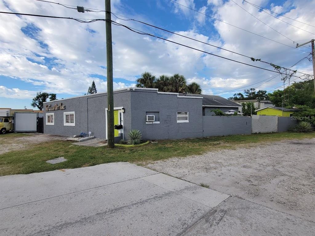 A gray commercial building with a lime green door stands next to a gravel lot — 5205 HAINES ROAD N, ST PETERSBURG, FL