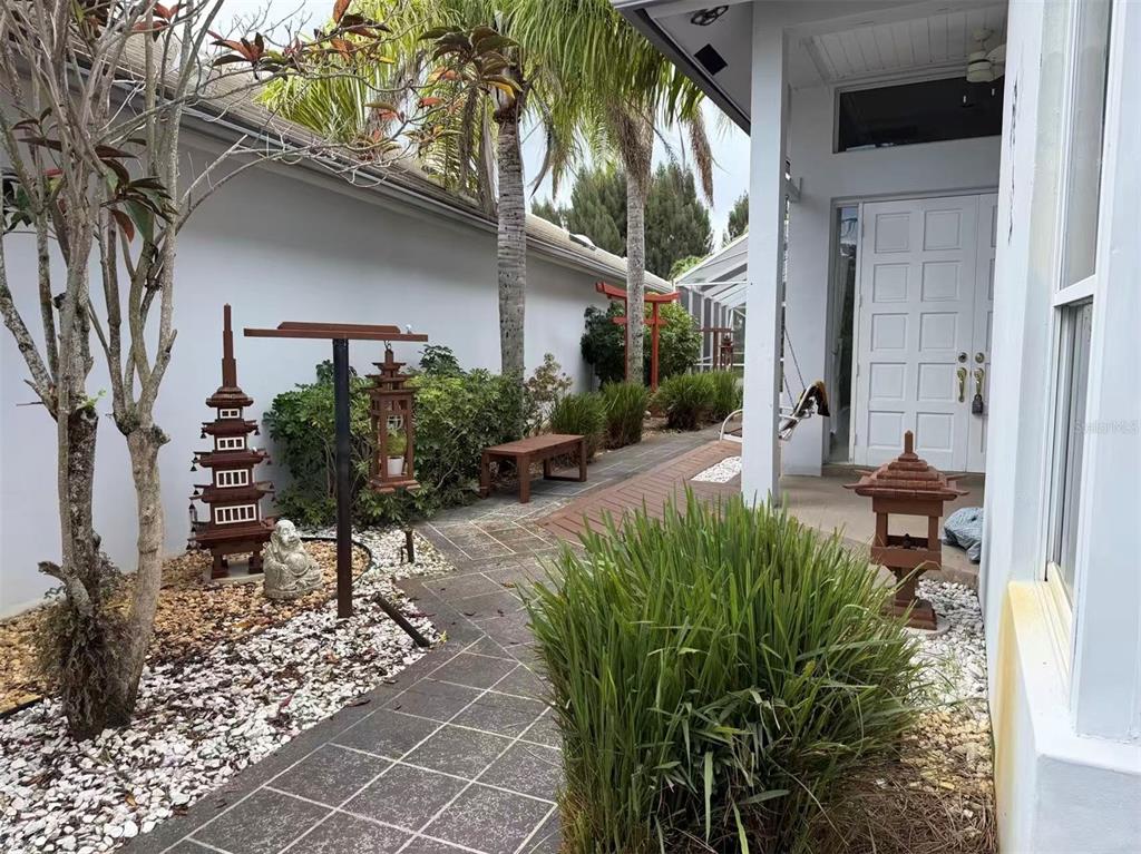 A tiled walkway leads to a white front door, featuring Japanese-style garden ornaments and landscaping — 173 ORANGE TREE DRIVE, ATLANTIS, FL