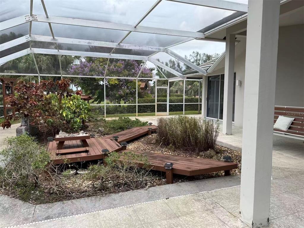 A screened-in patio features a wooden deck walkway, landscaping, and a hanging porch swing — 173 ORANGE TREE DRIVE, ATLANTIS, FL