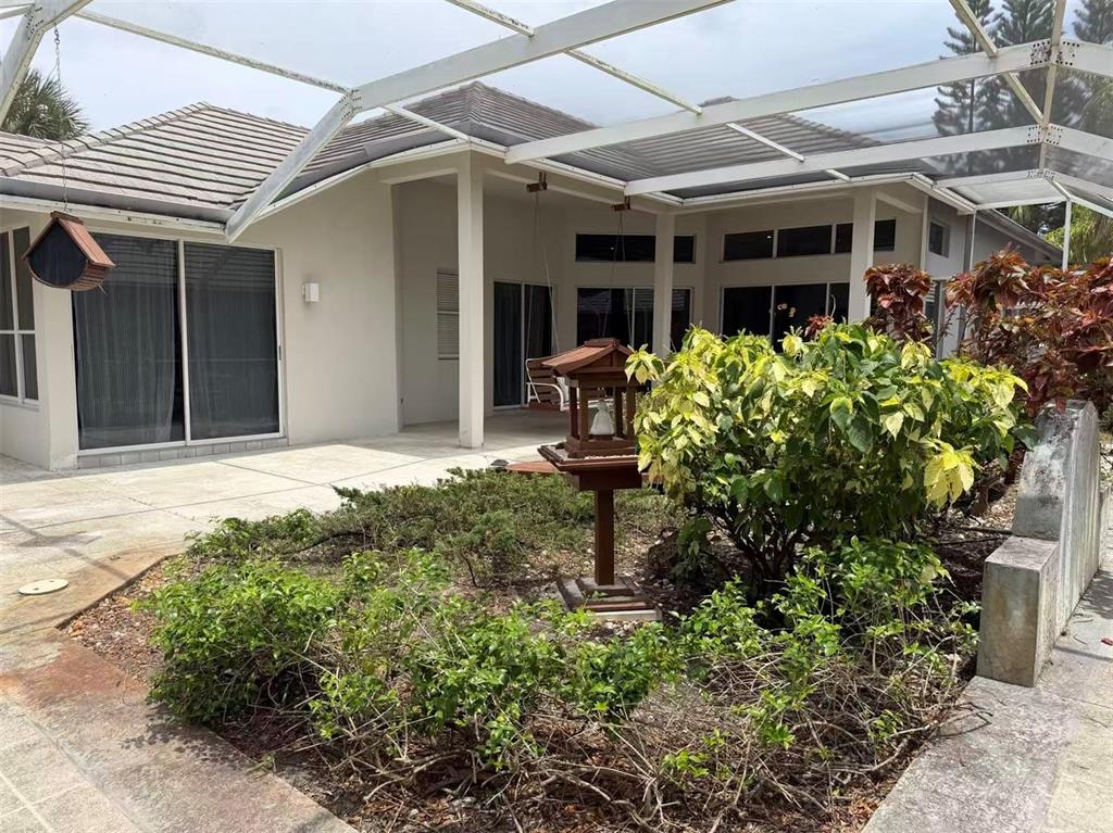 A screened-in patio features a concrete floor, a small garden bed, and a bird feeder — 173 ORANGE TREE DRIVE, ATLANTIS, FL