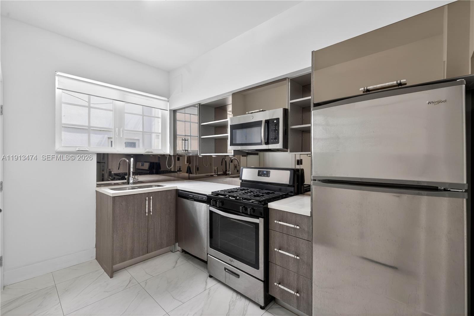 A modern kitchen features stainless steel appliances, wood-toned cabinetry, and a mirrored backsplash — 1601 Jefferson Ave, Miami Beach FL 33139, MIAMI BEACH, FL