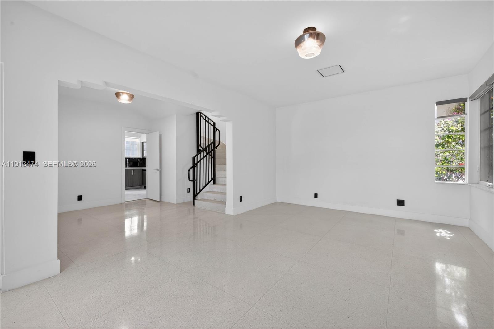 A bright, empty room features white walls, light tile flooring, and a black metal staircase — 1601 Jefferson Ave, Miami Beach FL 33139, MIAMI BEACH, FL
