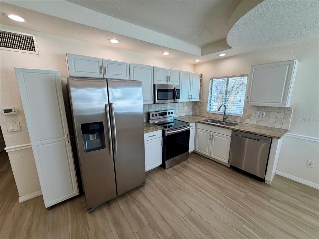 A kitchen features white cabinets, stainless steel appliances, granite countertops, and light wood-look flooring — 350 GULF BOULEVARD UNIT 1, INDIAN ROCKS BEACH, FL