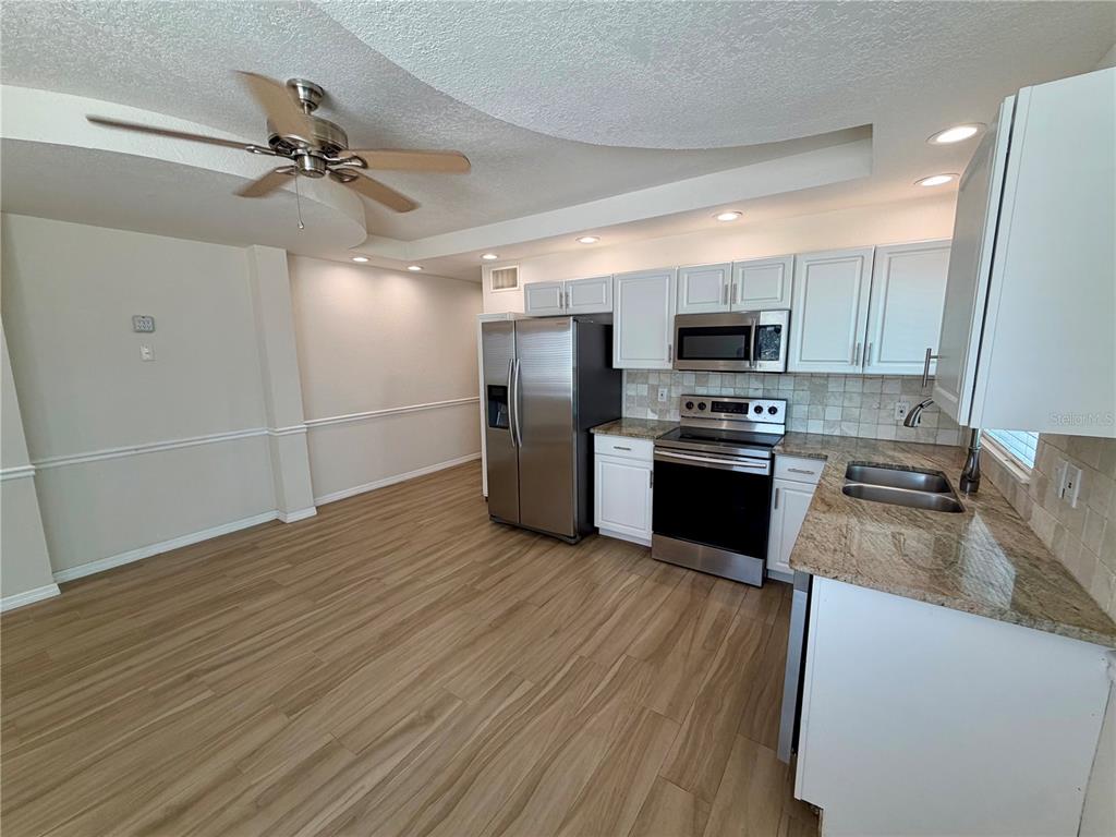 A kitchen features white cabinets, stainless steel appliances, granite countertops, and light wood-look flooring — 350 GULF BOULEVARD UNIT 1, INDIAN ROCKS BEACH, FL