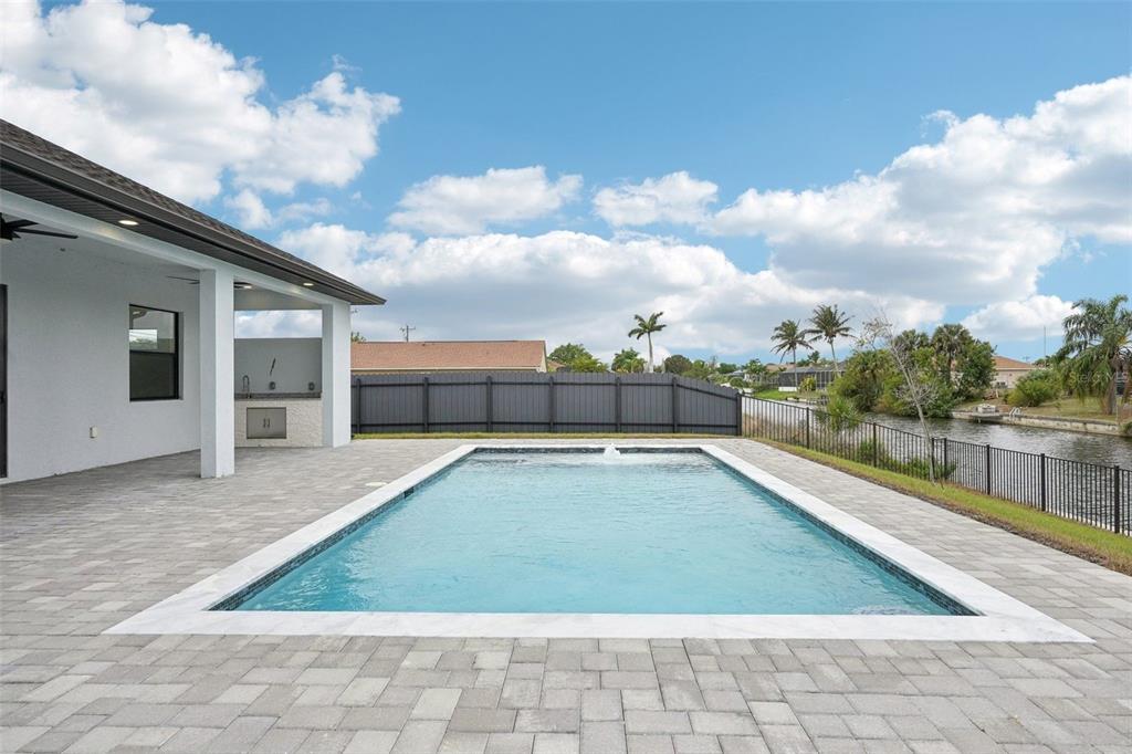 A rectangular swimming pool sits on a paved patio next to a house and canal — 12 SE 17TH AVENUE, CAPE CORAL, FL