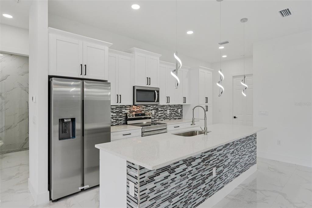 A modern kitchen features white cabinets, stainless steel appliances, and a tiled kitchen island — 12 SE 17TH AVENUE, CAPE CORAL, FL