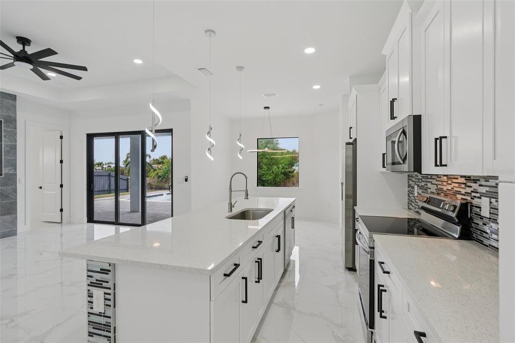 A modern white kitchen features a large quartz island, stainless steel appliances, and tile flooring — 12 SE 17TH AVENUE, CAPE CORAL, FL