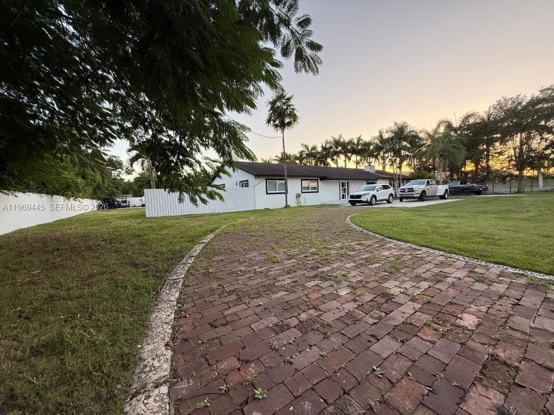 A white single-story house with a brick driveway and palm trees at sunset — 15750 SW 216th St, Miami FL 33170, MIAMI, FL