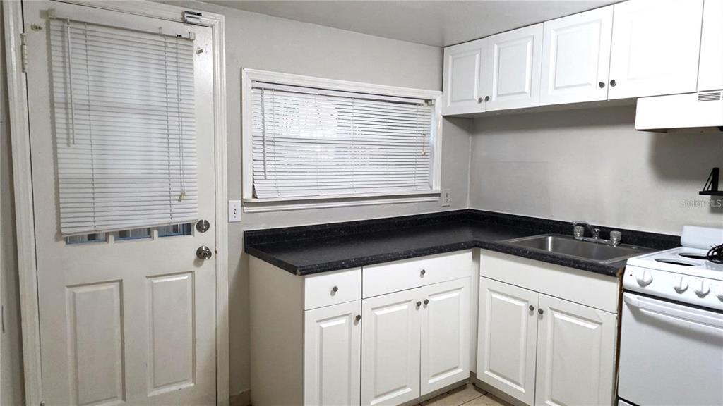 A kitchen features white cabinets, black countertops, a stainless steel sink, and a white stove — 1113 S PARK AVENUE, SANFORD, FL