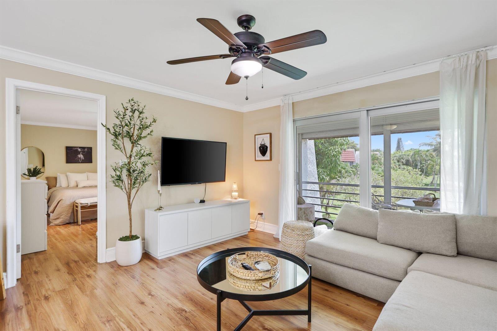 A living room features a ceiling fan, a wall-mounted television, and a sliding glass door — 2700 Fiore Way # 2020, Delray Beach FL 33445, DELRAY BEACH, FL