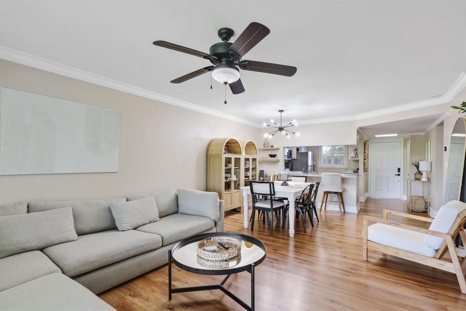 An open-concept living and dining area features a sectional sofa, wood floors, and ceiling fans — 2700 Fiore Way # 2020, Delray Beach FL 33445, DELRAY BEACH, FL
