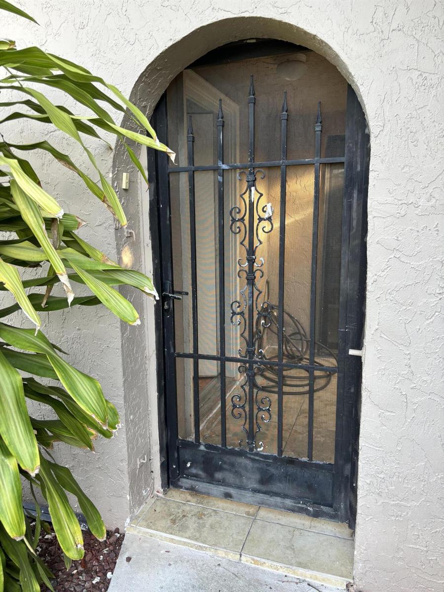 An arched black metal security screen door is installed in a stucco exterior wall — 12761 Westhampton Circle, Wellington FL 33414, WELLINGTON, FL