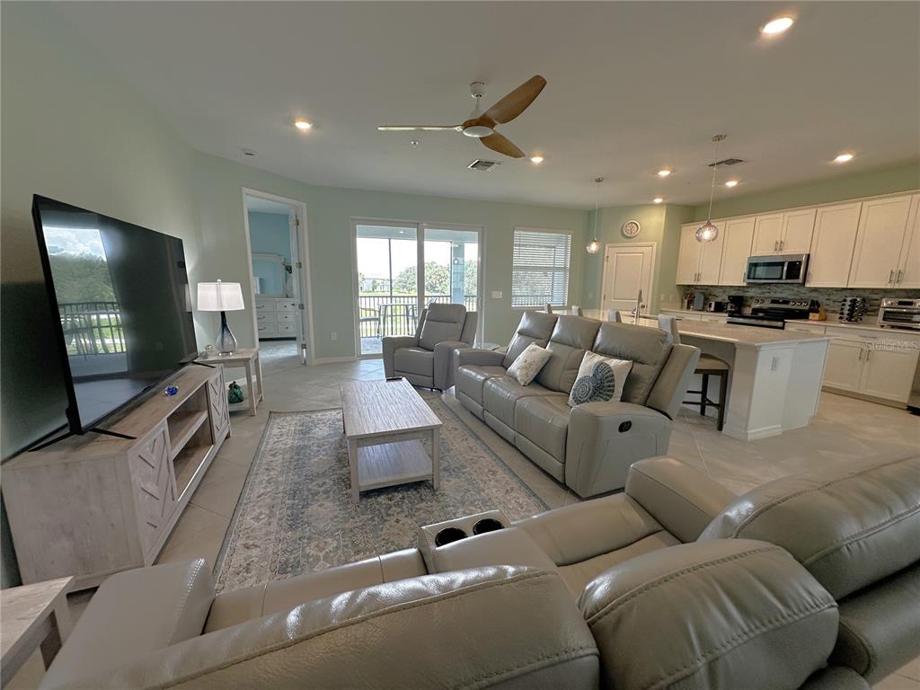 An open-concept living room and kitchen featuring light-colored cabinetry, gray leather furniture, and tile flooring — 4835 BIRCHWOOD COURT UNIT 6222, PUNTA GORDA, FL