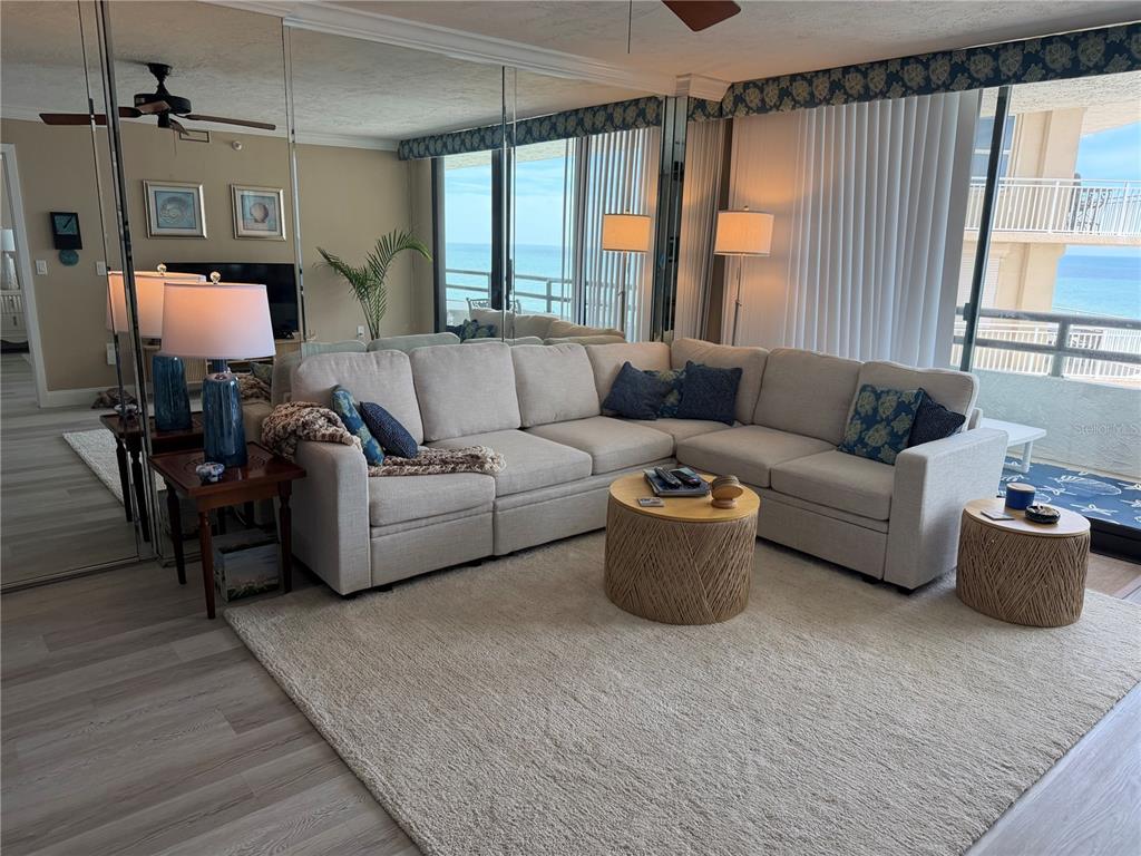 A living room features a beige sectional sofa, a round coffee table, and mirrored walls — 3855 S ATLANTIC AVENUE UNIT 702, DAYTONA BEACH, FL