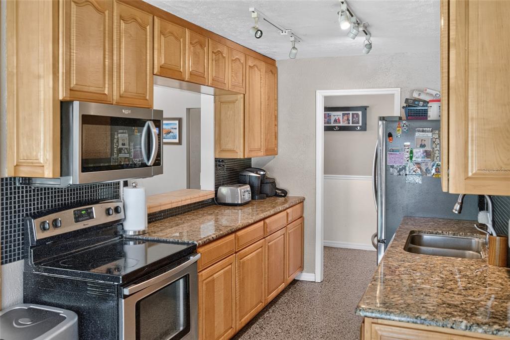 A kitchen features light wood cabinets, granite countertops, stainless steel appliances, and black tile backsplashes — 2420 HAZEL BISHOP DRIVE, NEW SMYRNA BEACH, FL