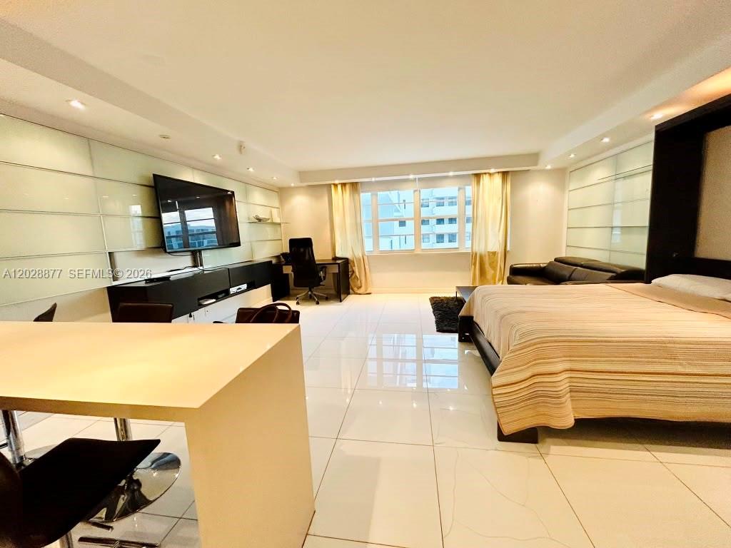 A modern bedroom features white tile floors, a large bed, a desk, and a television — 100 Lincoln Rd # 701, Miami Beach FL 33139, MIAMI BEACH, FL
