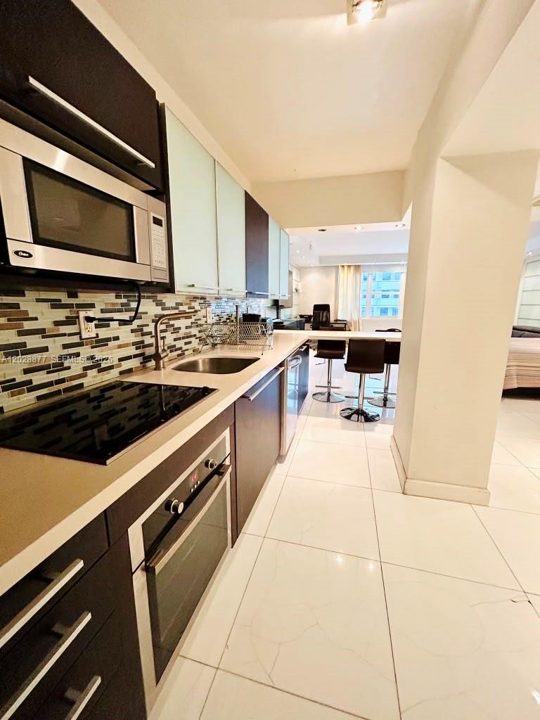A modern kitchen features dark cabinets, stainless steel appliances, and a tiled backsplash — 100 Lincoln Rd # 701, Miami Beach FL 33139, MIAMI BEACH, FL
