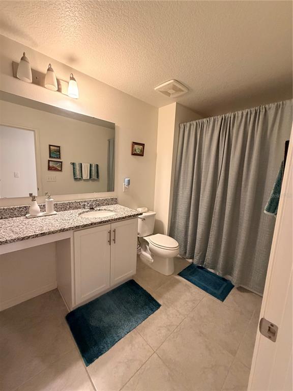 A bathroom features a granite vanity, white cabinets, a toilet, and a shower with curtains — 9051 OSCRAFT DRIVE, DAVENPORT, FL