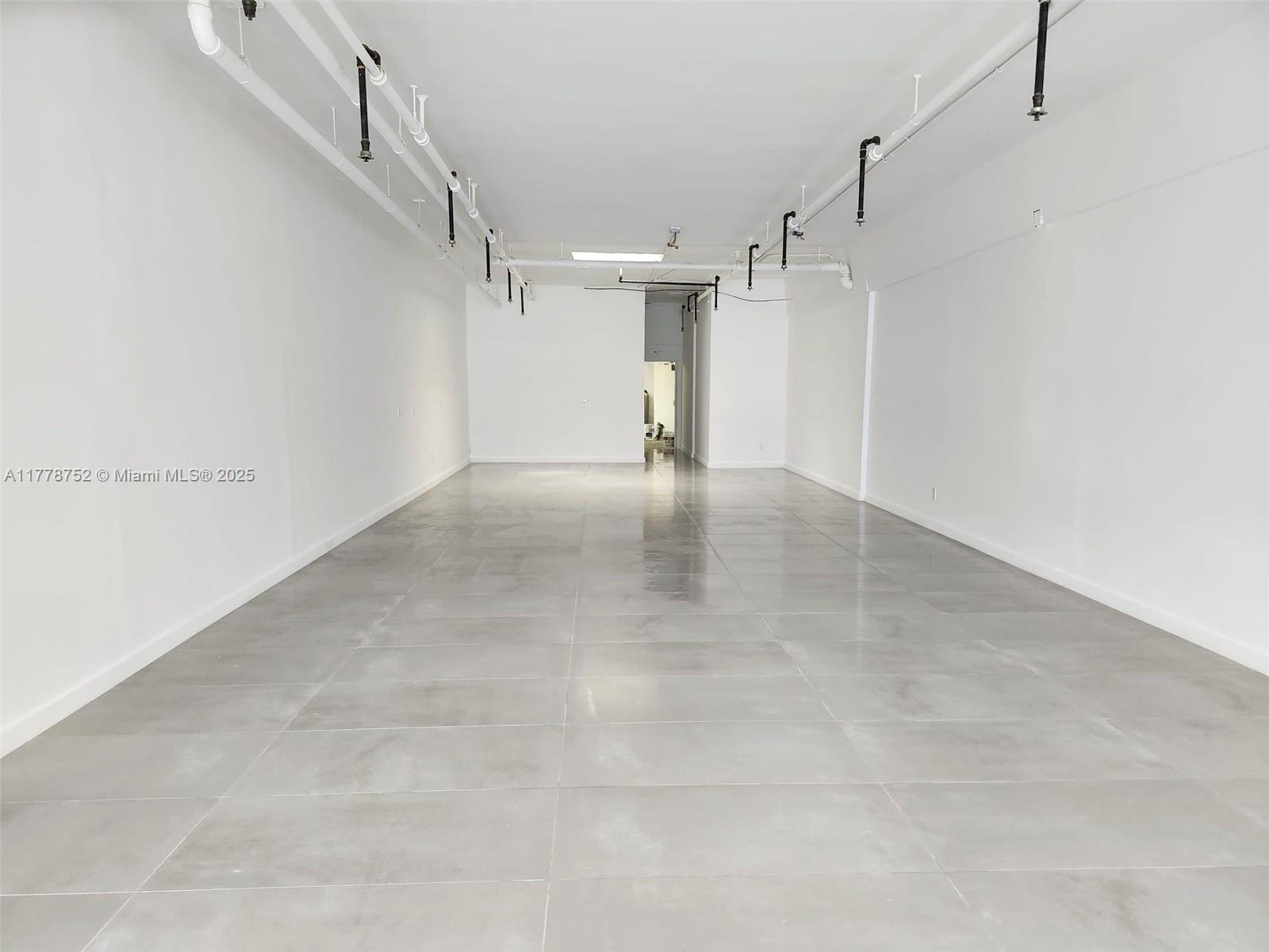 An empty commercial space features white walls, a gray tiled floor, and exposed ceiling pipes — 31 SW Osceola St, Stuart FL 34994, STUART, FL