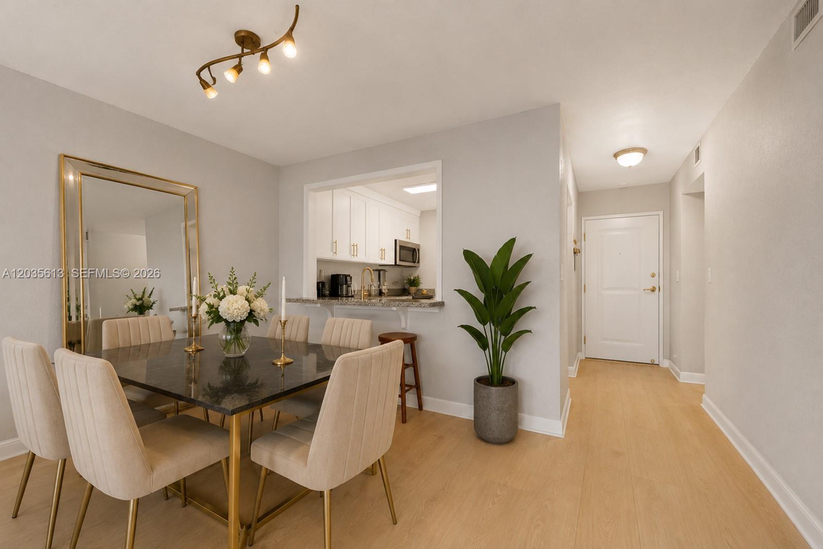 A dining area features a dark square table, upholstered chairs, a large mirror, and kitchen pass-through — 7845 Camino Real # 413, Miami FL 33143, MIAMI, FL