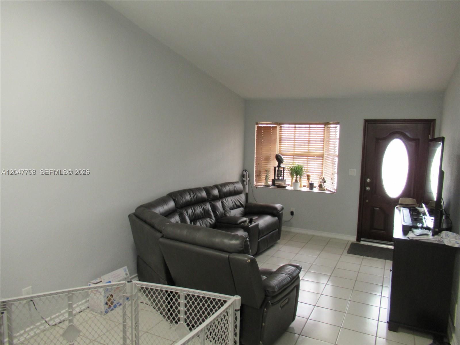 A living room features a dark leather sectional sofa, tiled floors, and a front door — 11530 NW 87th Ct, Hialeah Gardens FL 33018, HIALEAH GARDENS, FL