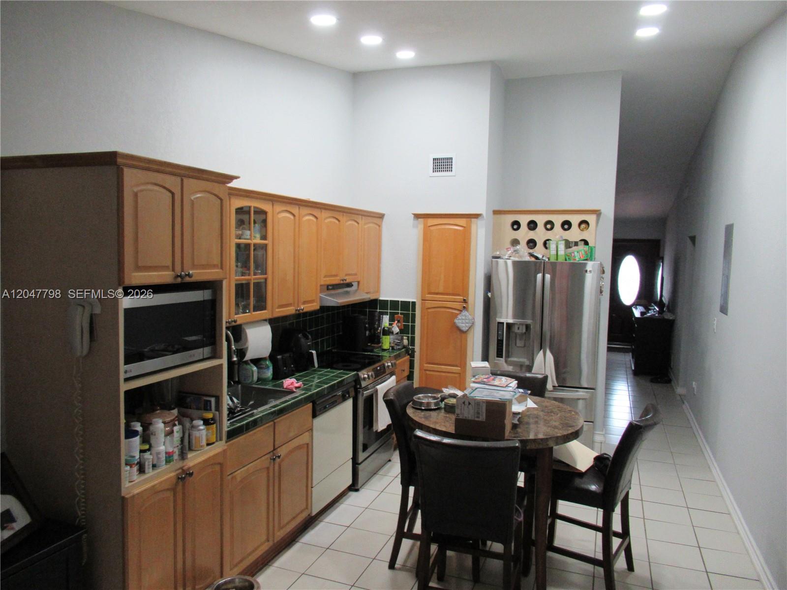 A kitchen features light wood cabinets, green tile countertops, stainless steel appliances, and a dining table — 11530 NW 87th Ct, Hialeah Gardens FL 33018, HIALEAH GARDENS, FL