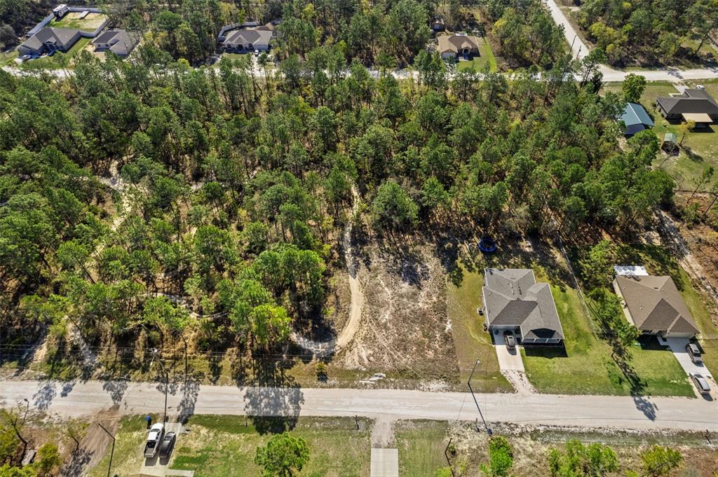 An aerial view shows a vacant residential lot surrounded by trees next to two houses — 12348 SNOWY EGRET AVENUE, WEEKI WACHEE, FL
