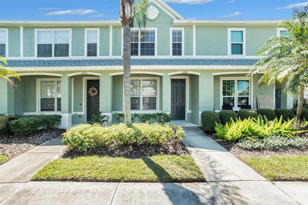 A two-story townhouse with light green siding, dark doors, and a landscaped front yard — 11676 DECLARATION DRIVE, TAMPA, FL