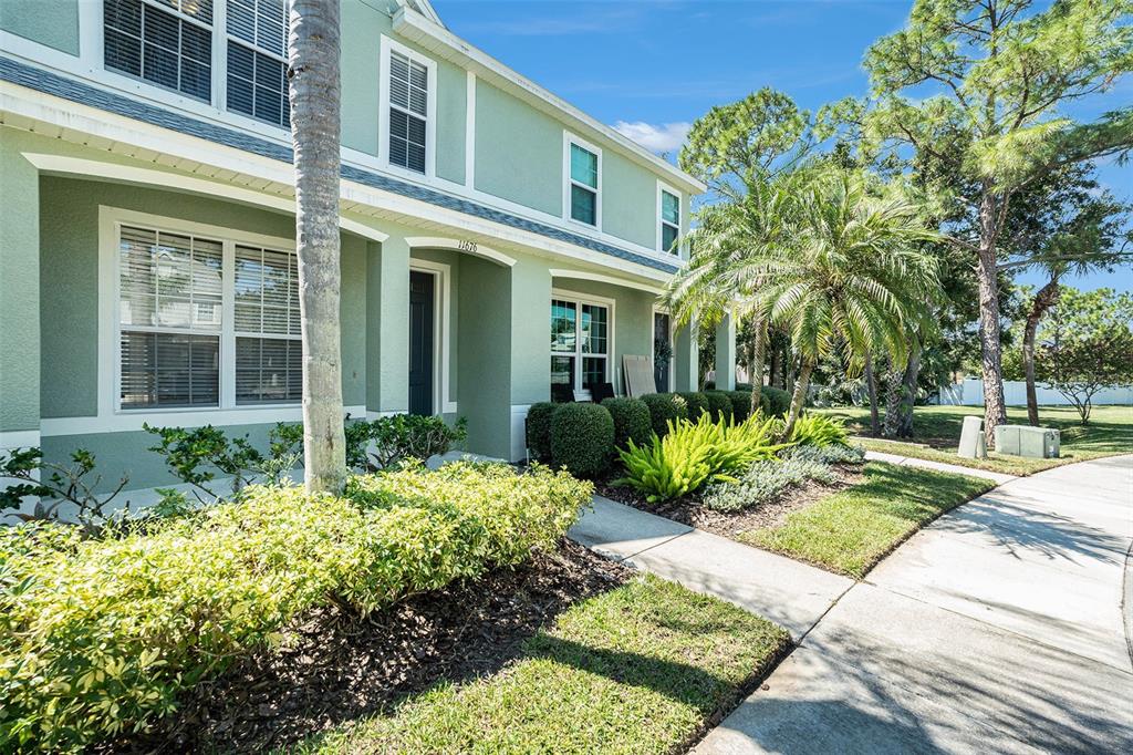 A light green two-story townhouse features white trim, large windows, and landscaped front gardens — 11676 DECLARATION DRIVE, TAMPA, FL