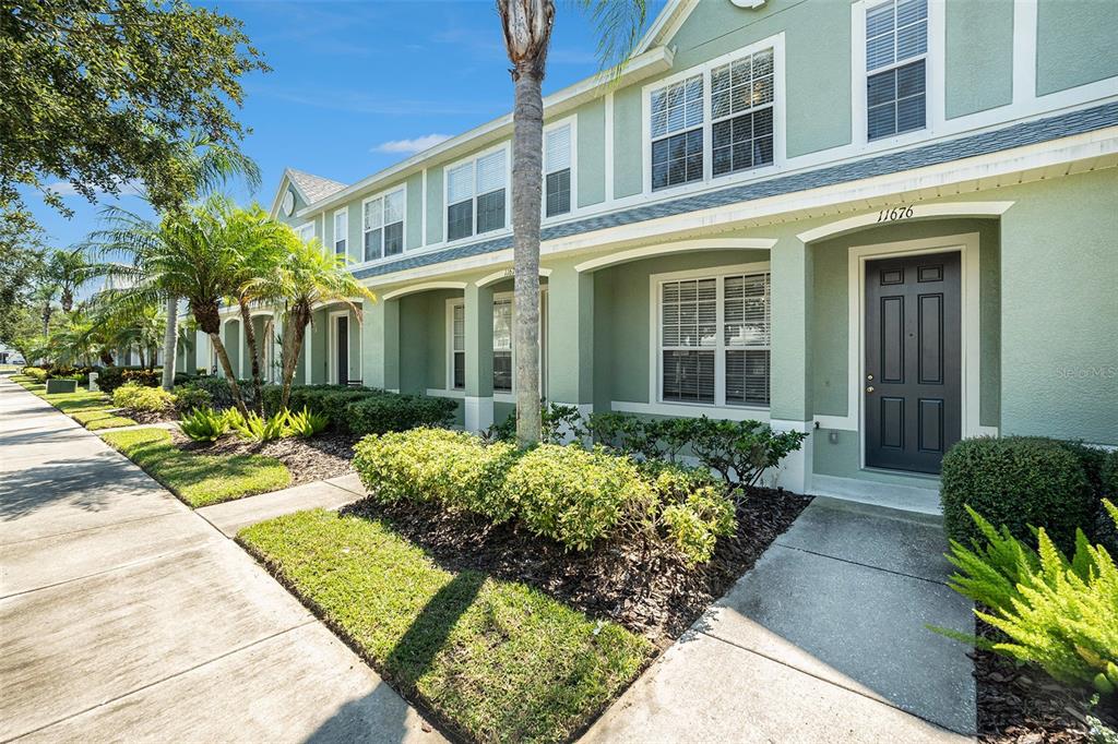 A light green townhome exterior features a dark front door, white trim, and landscaping — 11676 DECLARATION DRIVE, TAMPA, FL