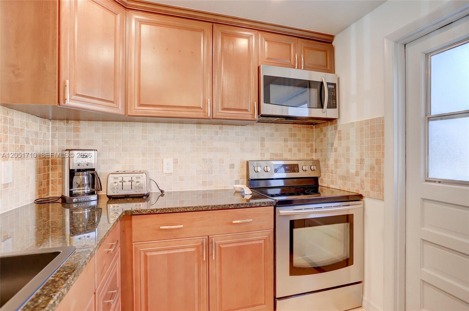 A kitchen features wooden cabinets, granite countertops, stainless steel appliances, and a tiled backsplash — 2212 NE 1st Way # 101, Boynton Beach FL 33435, BOYNTON BEACH, FL
