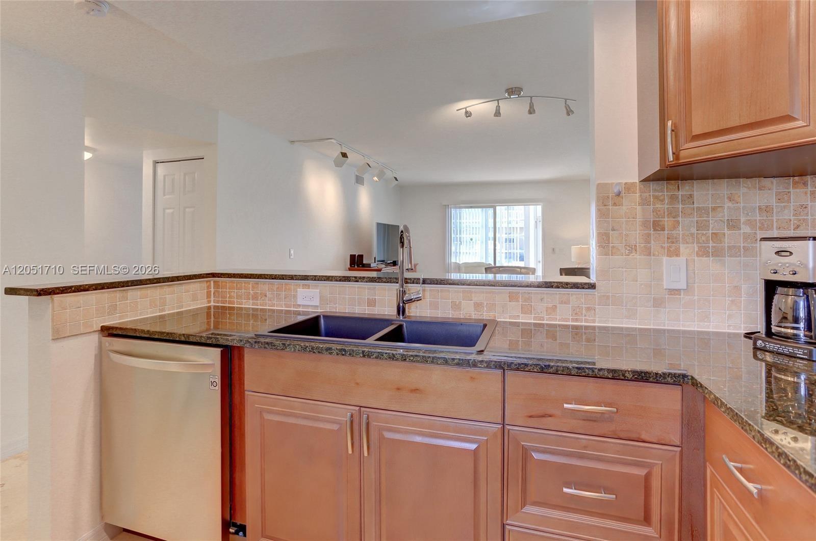 A kitchen features wood cabinets, dark granite countertops, a double sink, and a tiled backsplash — 2212 NE 1st Way # 101, Boynton Beach FL 33435, BOYNTON BEACH, FL