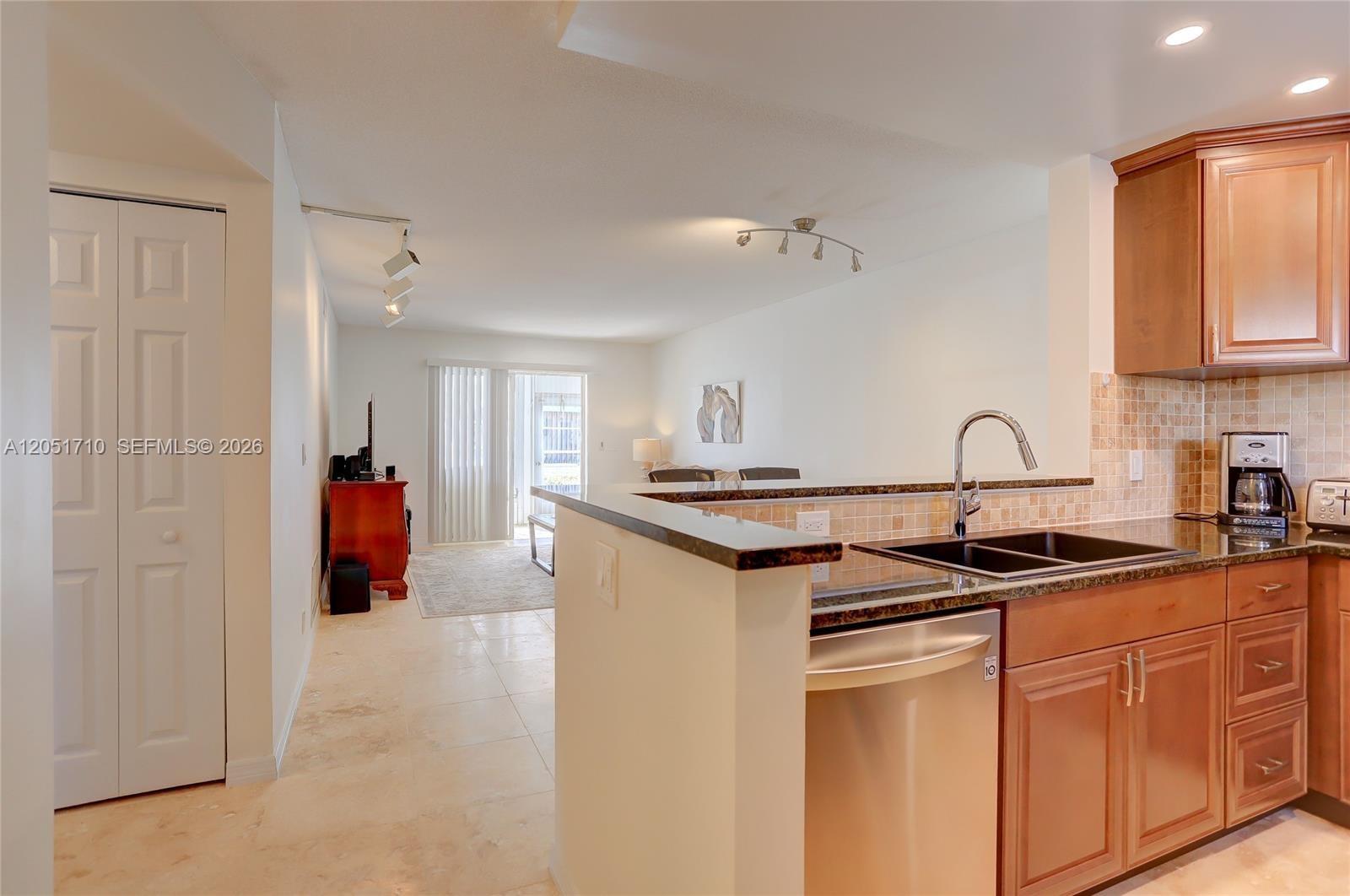 A kitchen with wood cabinets and granite countertops overlooks an open living area — 2212 NE 1st Way # 101, Boynton Beach FL 33435, BOYNTON BEACH, FL