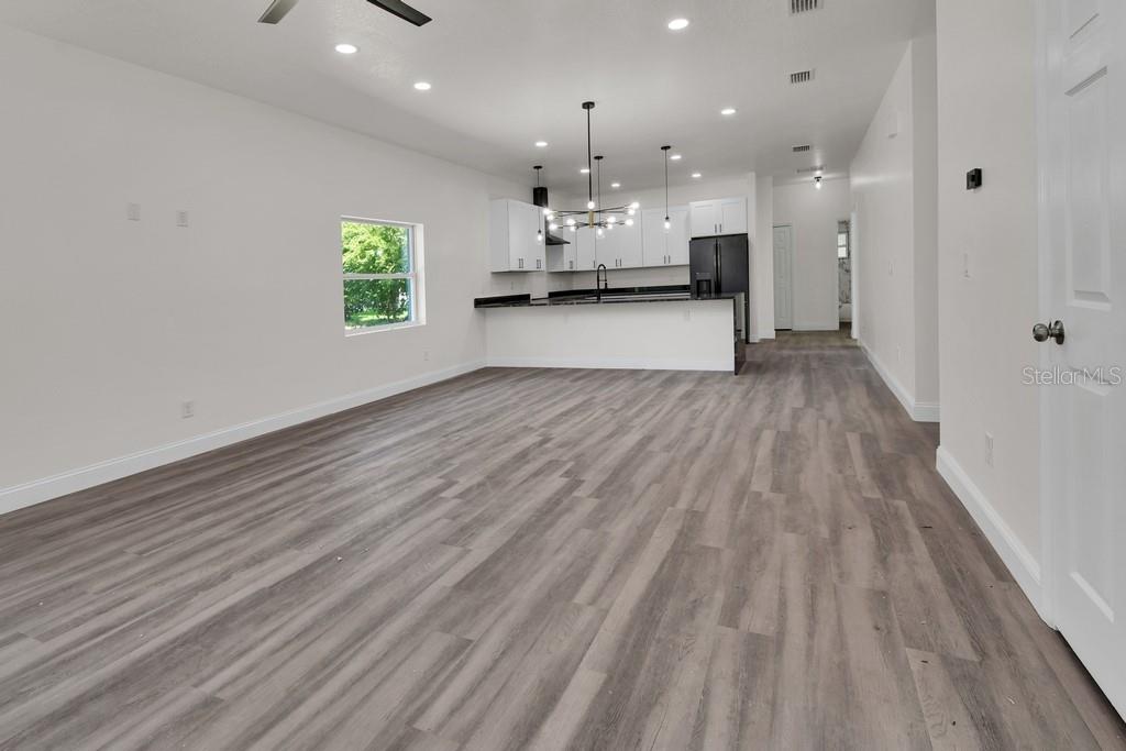 An open-concept kitchen and living area features white cabinetry, black countertops, and wood-look flooring — 558 WALLACE STREET, DAYTONA BEACH, FL