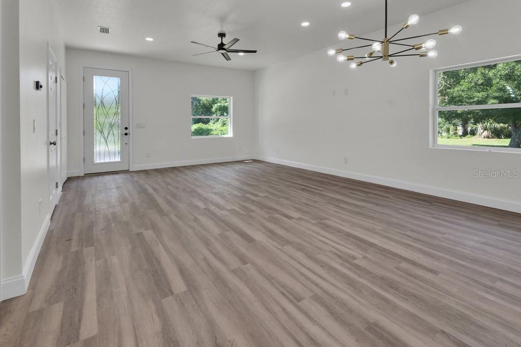 A bright, empty living room features light wood-look flooring, a ceiling fan, and modern lighting — 558 WALLACE STREET, DAYTONA BEACH, FL
