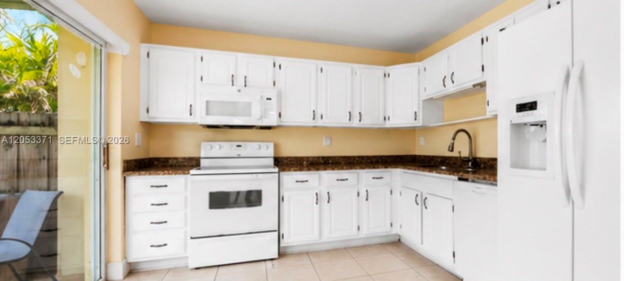 A kitchen with white cabinets, dark countertops, white appliances, and a sliding glass door — MIAMI, FL