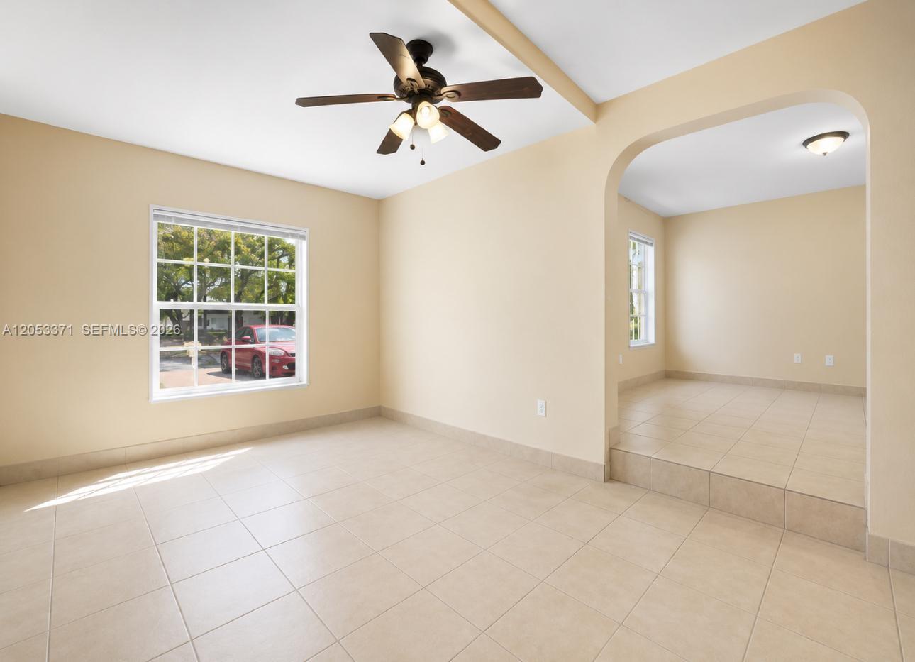 A beige room with tile flooring, a ceiling fan, and a raised adjacent area — MIAMI, FL