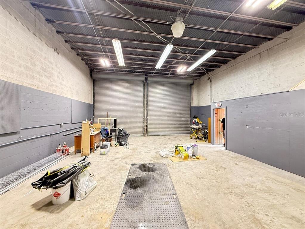 An industrial warehouse space features concrete walls, a metal ceiling, and two large roll-up doors — 14040 NW 19TH AVENUE, OPA LOCKA, FL