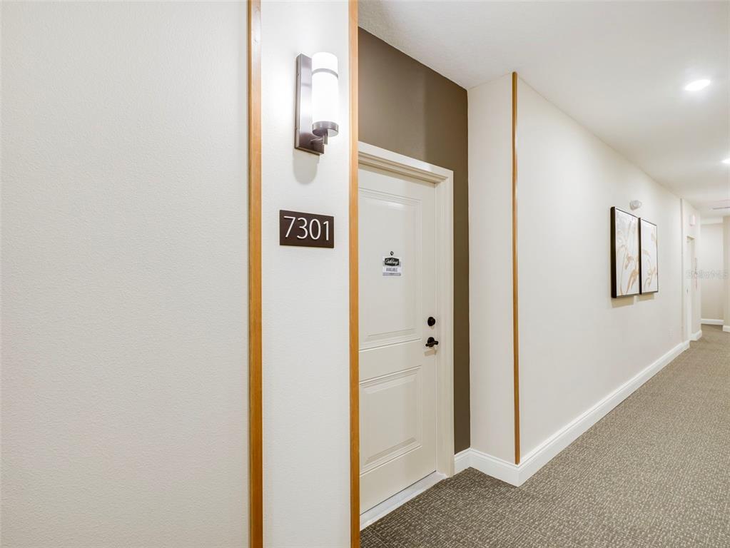 A hallway features a white door labeled 7301, a wall sconce, and carpeted flooring — 7545 LAUREATE BOULEVARD UNIT 7301, ORLANDO, FL